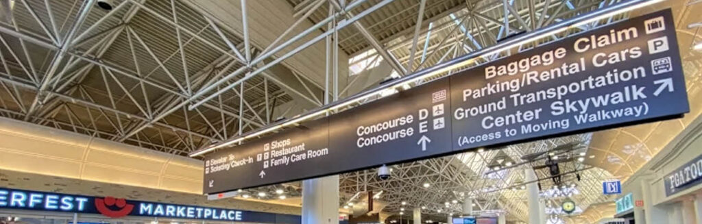 Airport wayfinding sign inside Milwaukee Mitchell International Airport directing travelers to baggage claim, parking, rental cars, ground transportation, concourses, and skywalk.